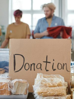 Volunteers sort clothes and food in a donation center. Cardboard sign reads 'Donation.'